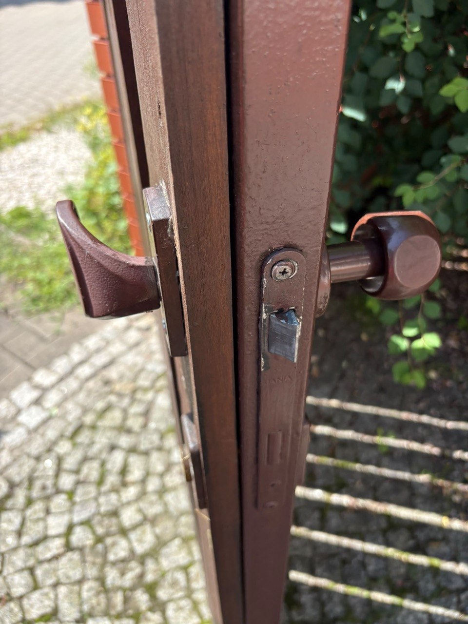 Zamek wpuszczany w metalowej furtce — zapadka, klamki i mocowanie listwy