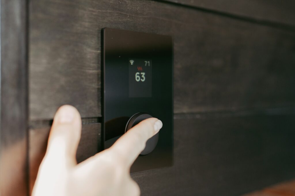 Dłoń ustawiająca inteligentny termostat na ścianie nowoczesnego wnętrza – przykład urządzenia montowanego w Smart Home
