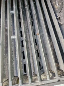 Pręty rusztu nad metalowym elementem z podłużnymi szczelinami