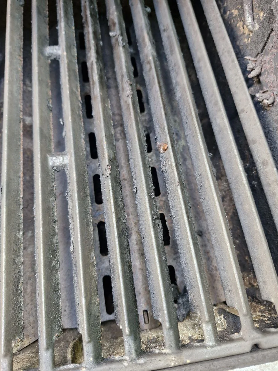 Pręty rusztu nad metalowym elementem z podłużnymi szczelinami